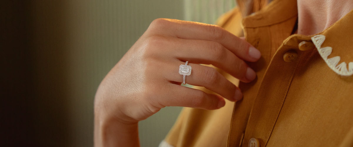 Bague à diamant taille émeraude entouré de petits diamants, portée à la main
