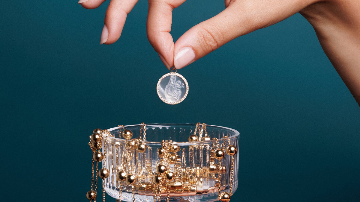 Main tenant une médaille ronde claire au-dessus d’une coupe en verre remplie de chaînes à boules