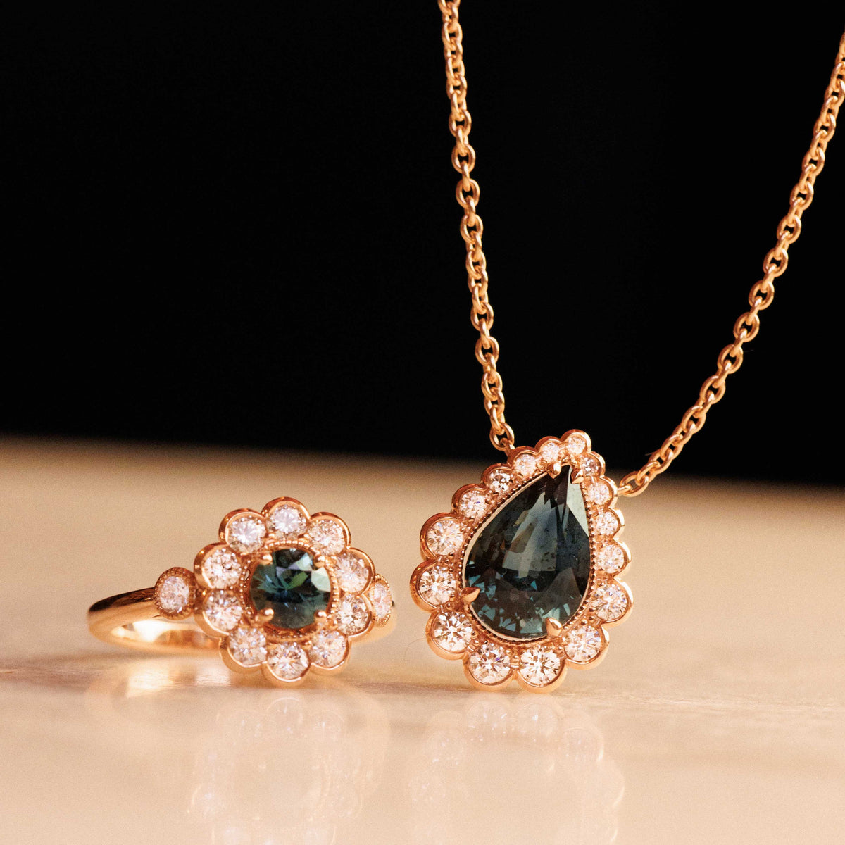Pendentif pompadour saphir vert or rose et diamants posé sur une table à côté d'une bague or rose diamants et saphir vert
