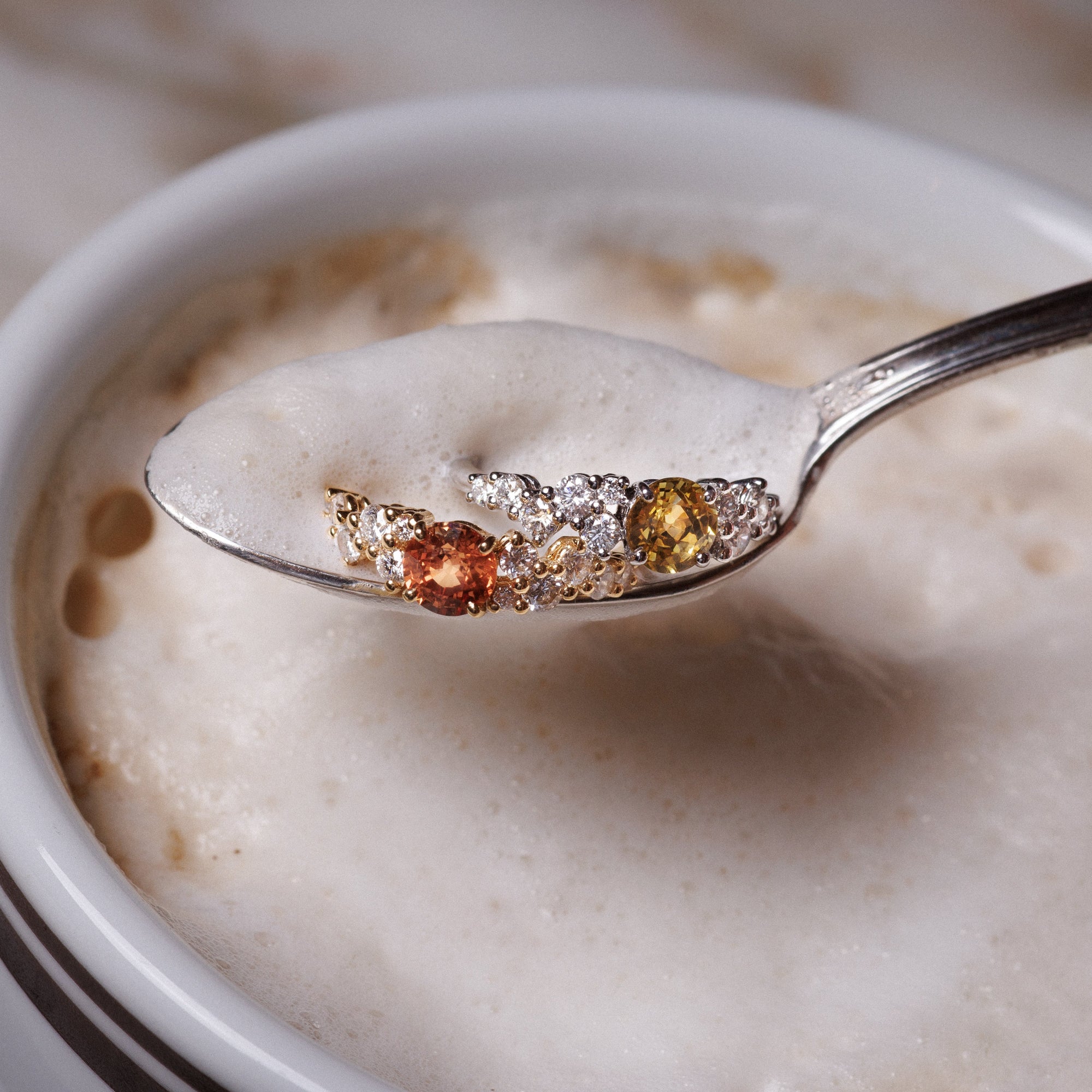 bague nuage saphir orange et saphir jaune posée dans une cuillère au dessus d'un café 