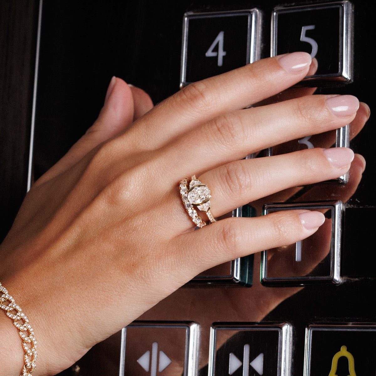 Main sur les boutons d’un ascenseur, portant la bague Cadillac et une alliance pavée