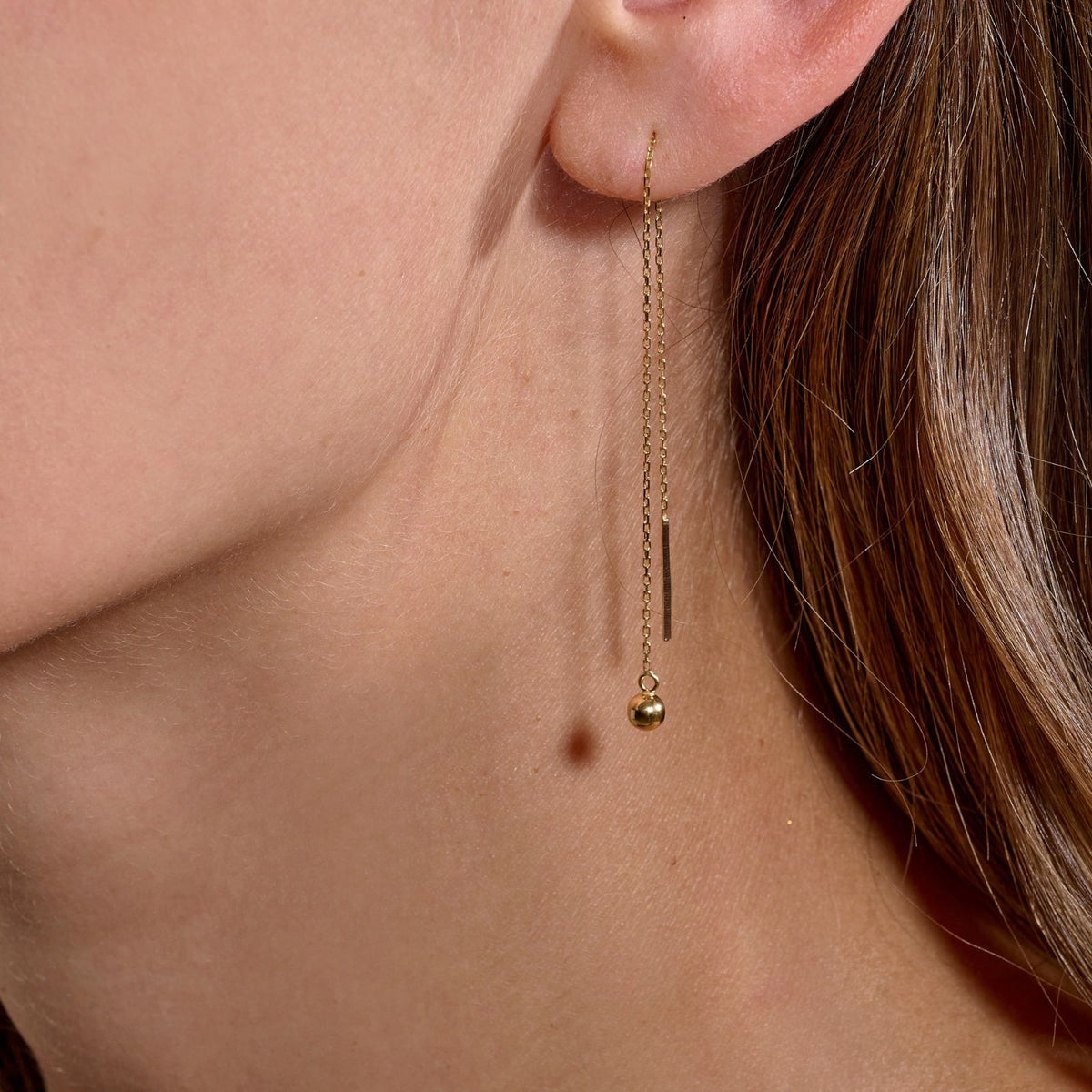 Oreille de femme portant une boucle d’oreille Marseillaises dansantes, chaîne fine passante et petite boule
