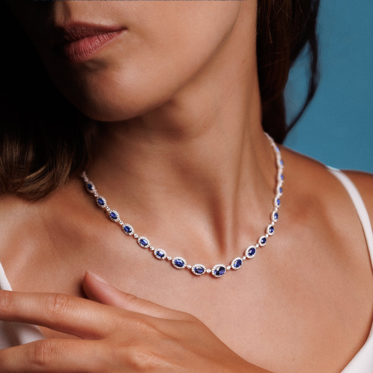 Cou de femme portant le collier Rivière saphirs et diamants, une main posée sur la clavicule